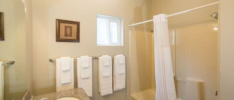 A bathroom with a granite sink, a large mirror, a framed picture on the wall, a window, and a glass-enclosed shower area.