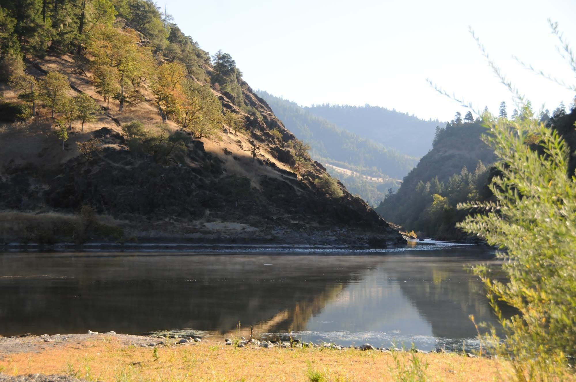 A river with a rocky riverbank and forested hills in the background.