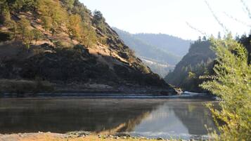 A river with a rocky riverbank and forested hills in the background.