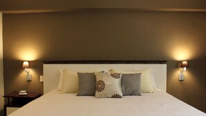 A neatly made bed with a headboard, two bedside lamps, and a small table with a cup and saucer.