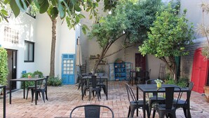 An outdoor patio with multiple tables and chairs, surrounded by greenery and potted plants.