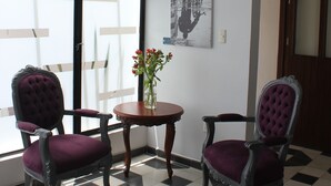 A room with two chairs, a table with a vase of flowers, and a large window with blinds.