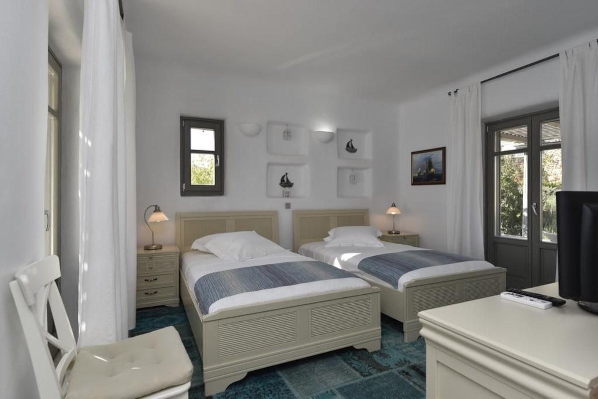 A hotel room with two beds, a desk, a chair, a television, and artwork on the walls.