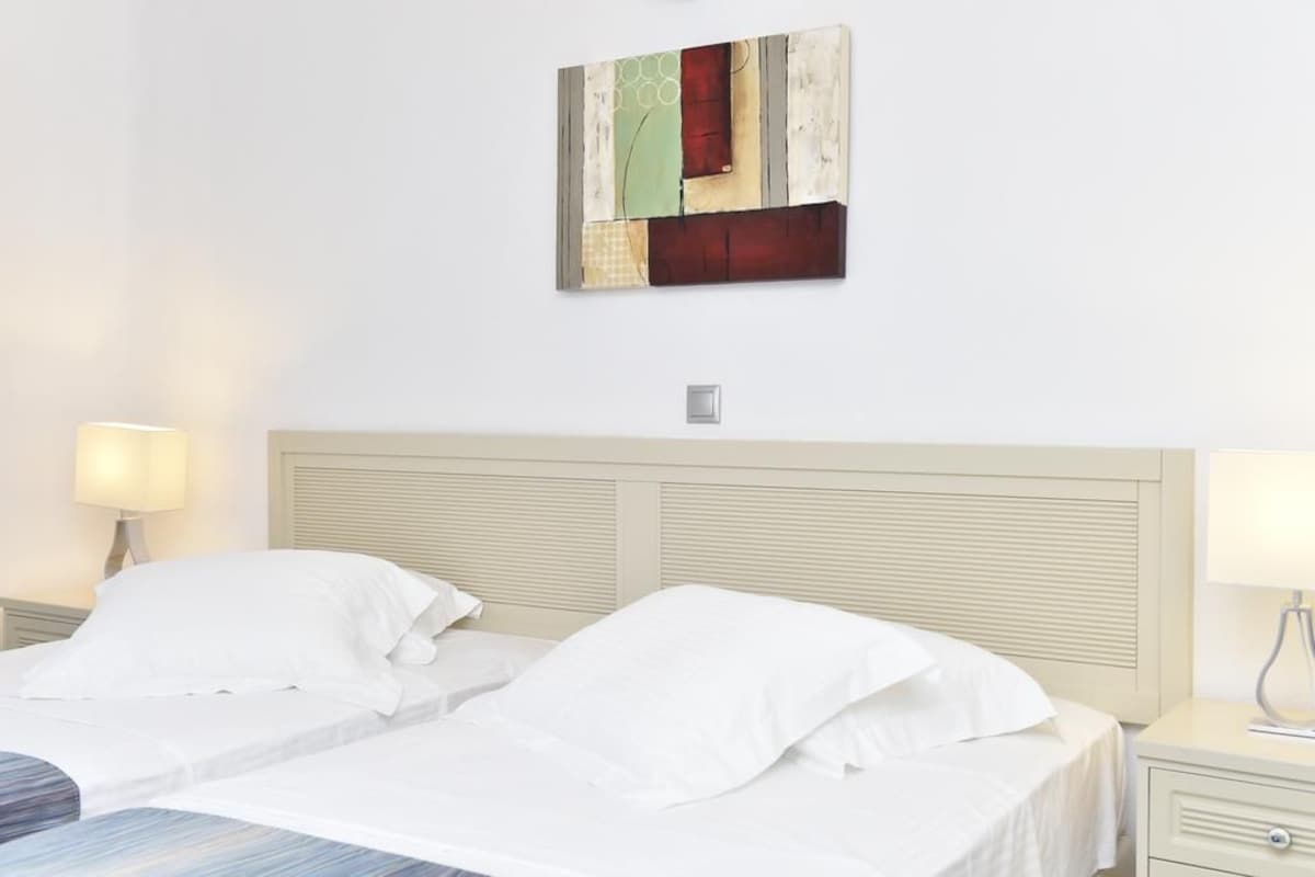 A hotel room with two beds, a headboard, bedside lamps, and a wall-mounted artwork.