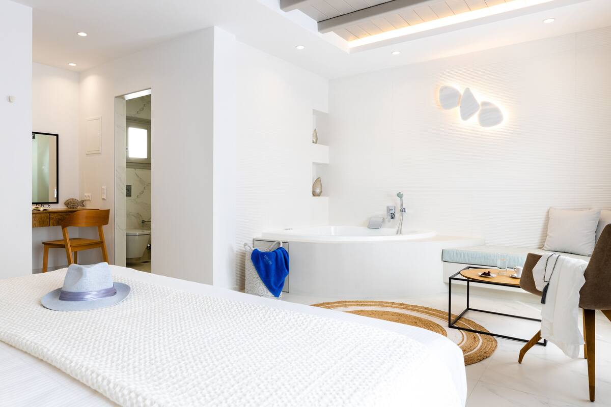 Une chambre d’hôtel moderne dotée d’un grand lit, d’un coin salon avec une table et un canapé, ainsi que d’une salle de bain avec un lavabo et un miroir.