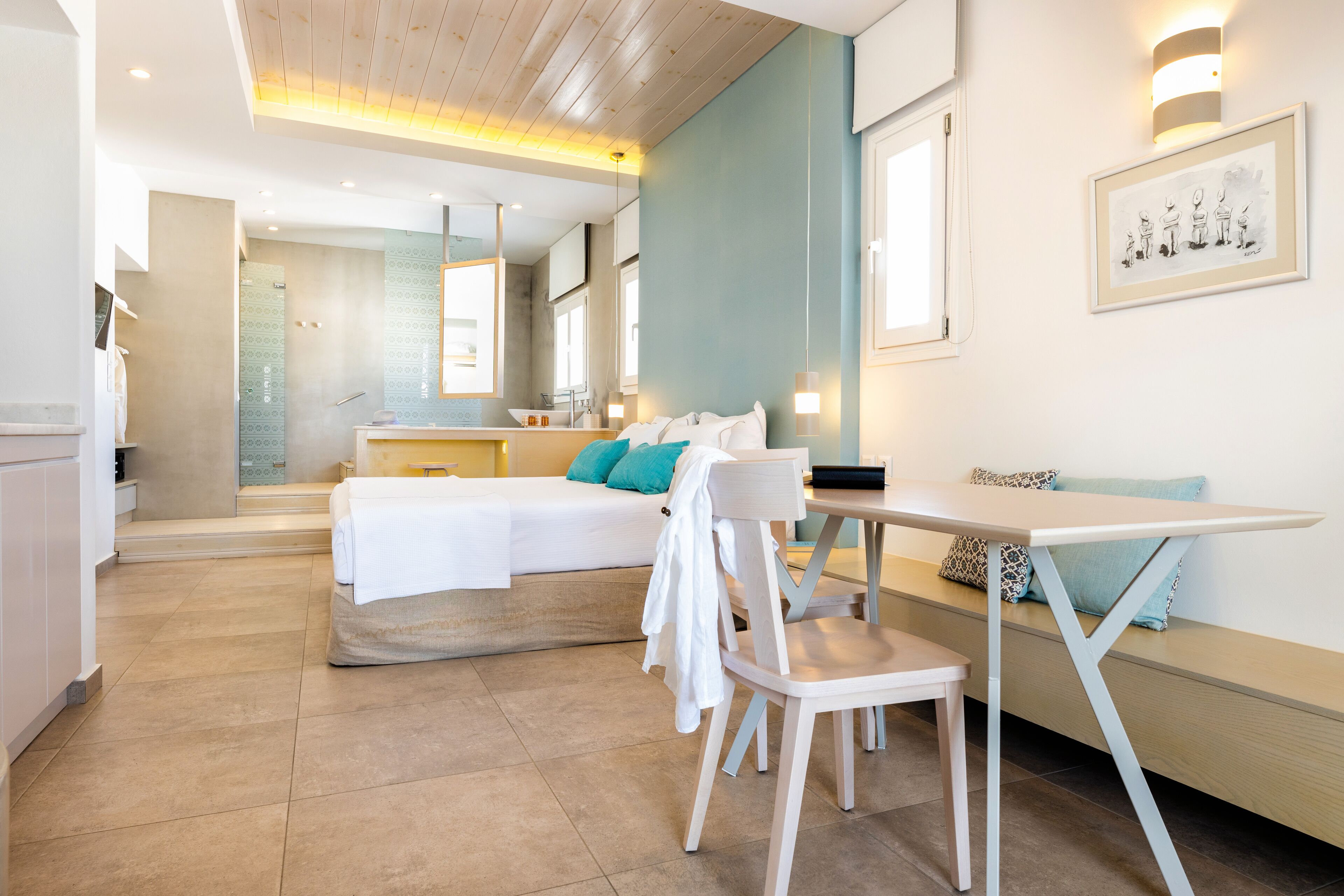 Una habitación de hotel moderna con una cama, un escritorio y un banco. Incluye un baño con ducha y lavamanos.