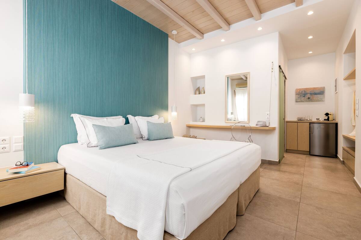 Une chambre moderne avec un grand lit, des tables de chevet, un miroir, une petite kitchenette et une salle de bain.