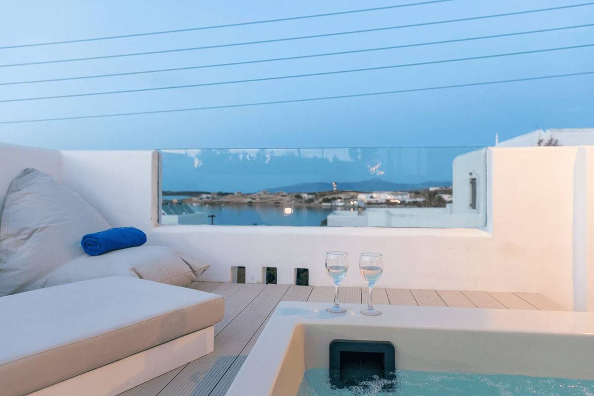 Un balcon avec un canapé blanc, une serviette bleue et un jacuzzi, avec deux verres d’eau à proximité.