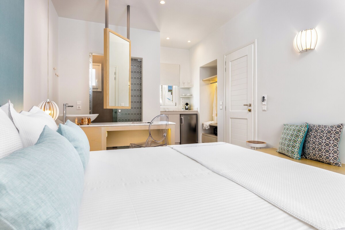 A modern hotel room with a large bed, a desk, and a kitchenette.