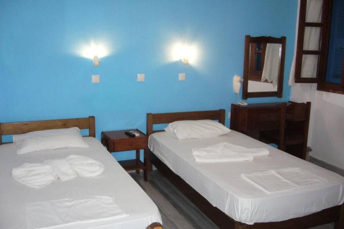 Two single beds with white linens, a wooden nightstand, a mirror, and a blue wall.
