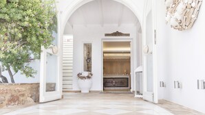 A spacious hallway with a checkered floor, leading to a kitchen area with wooden cabinets and a modern light fixture. - Stelia Mare Boutique Hotel (Paros)
