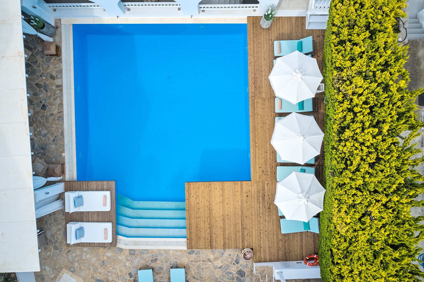 A rectangular swimming pool with a wooden deck area, surrounded by lounge chairs and umbrellas.