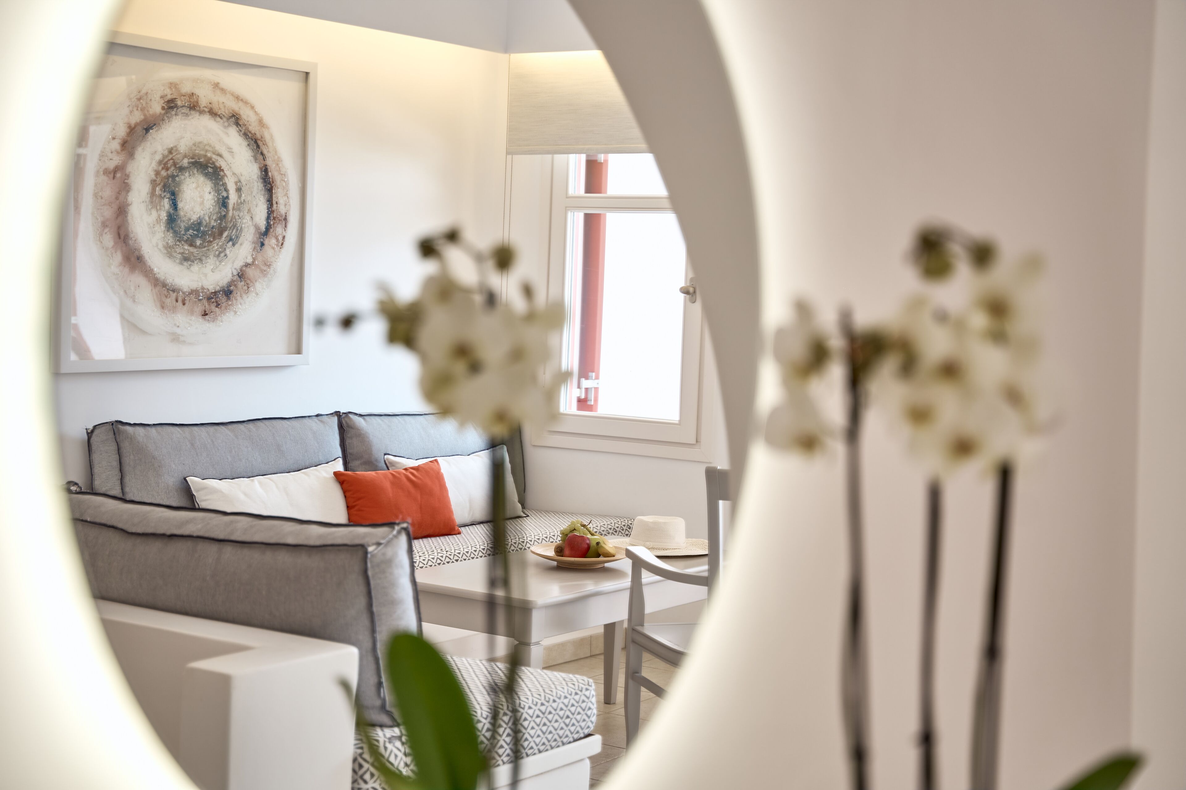 A modern living room with a grey sofa, a dining table with a fruit plate, and a large abstract painting on the wall.