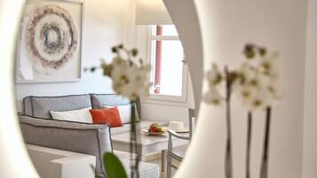 A modern living room with a grey sofa, a dining table with a fruit plate, and a large abstract painting on the wall.