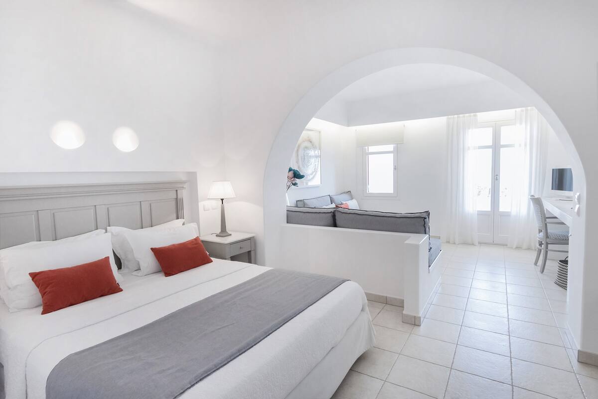 A hotel room with a large bed, a desk, and a view through an arched doorway.