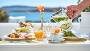 Una escena de desayuno con una mesa, platos, vasos y una persona sirviendo agua.
