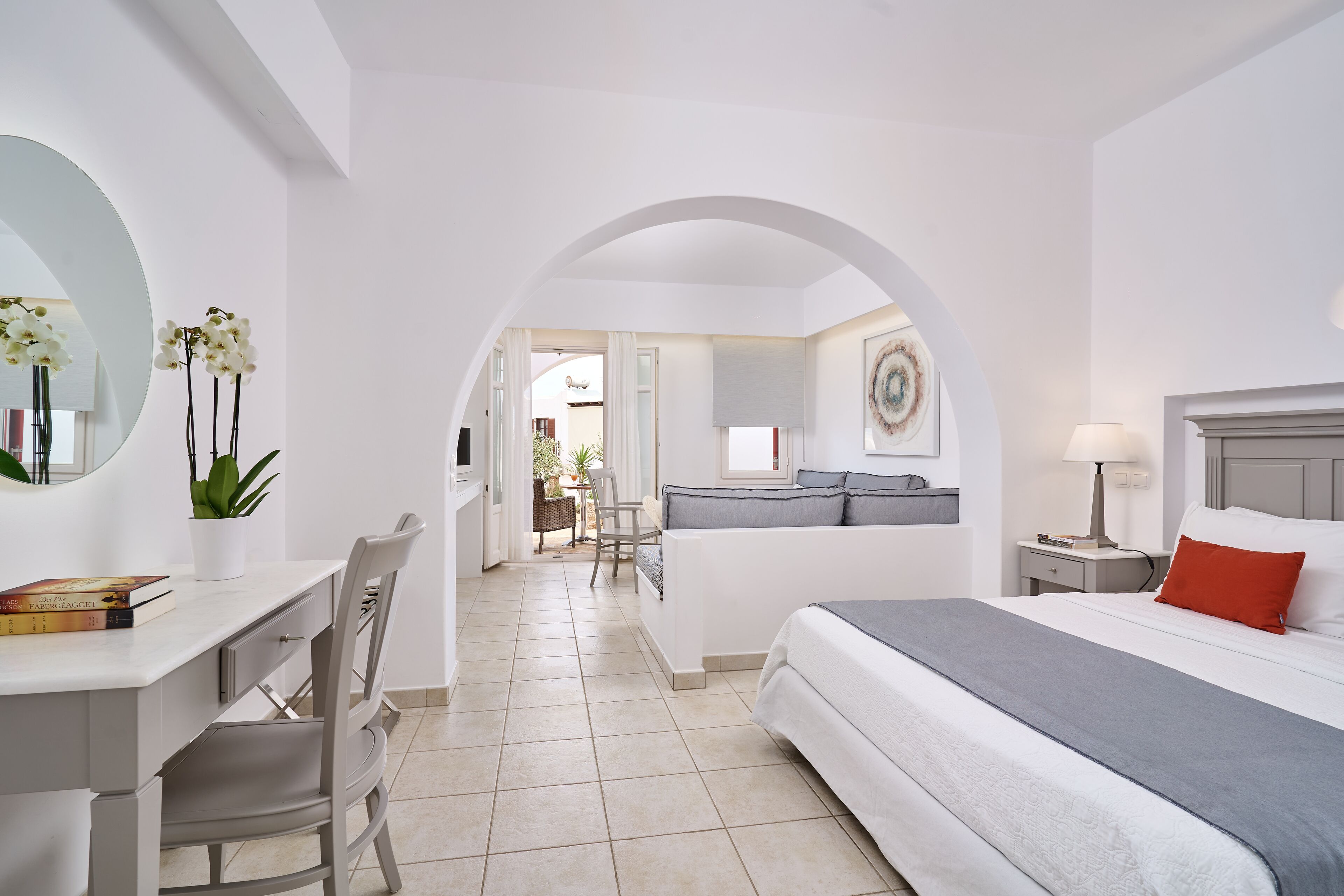 A modern hotel room with a bed, desk, chair, and a view of the dining area.
