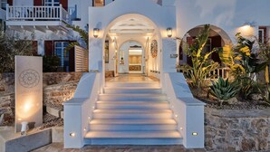A hotel entrance with a staircase leading to the main building, surrounded by stone walls and tropical plants. - Stelia Mare Boutique Hotel (Paros)