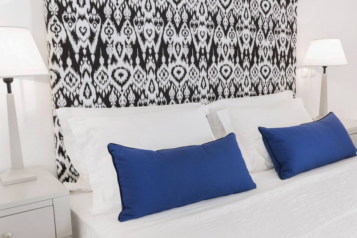 A neatly made bed with white and blue pillows, a patterned headboard, and two bedside lamps on a white nightstand.