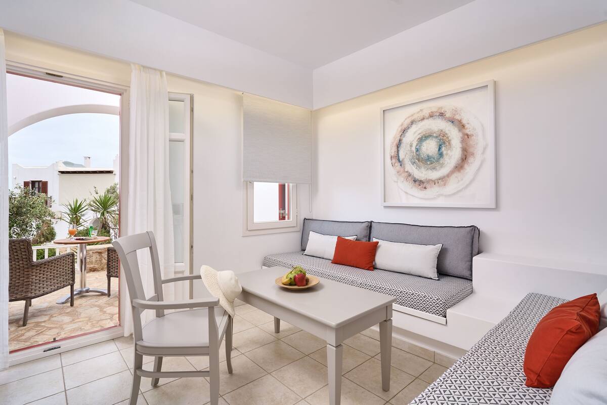 A modern living room with a white sofa, a dining table, and a large window.
