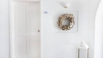 En hvid dør, en vægmonteret lampe, en billedramme med en krans, og en lille hvid lanterne.
