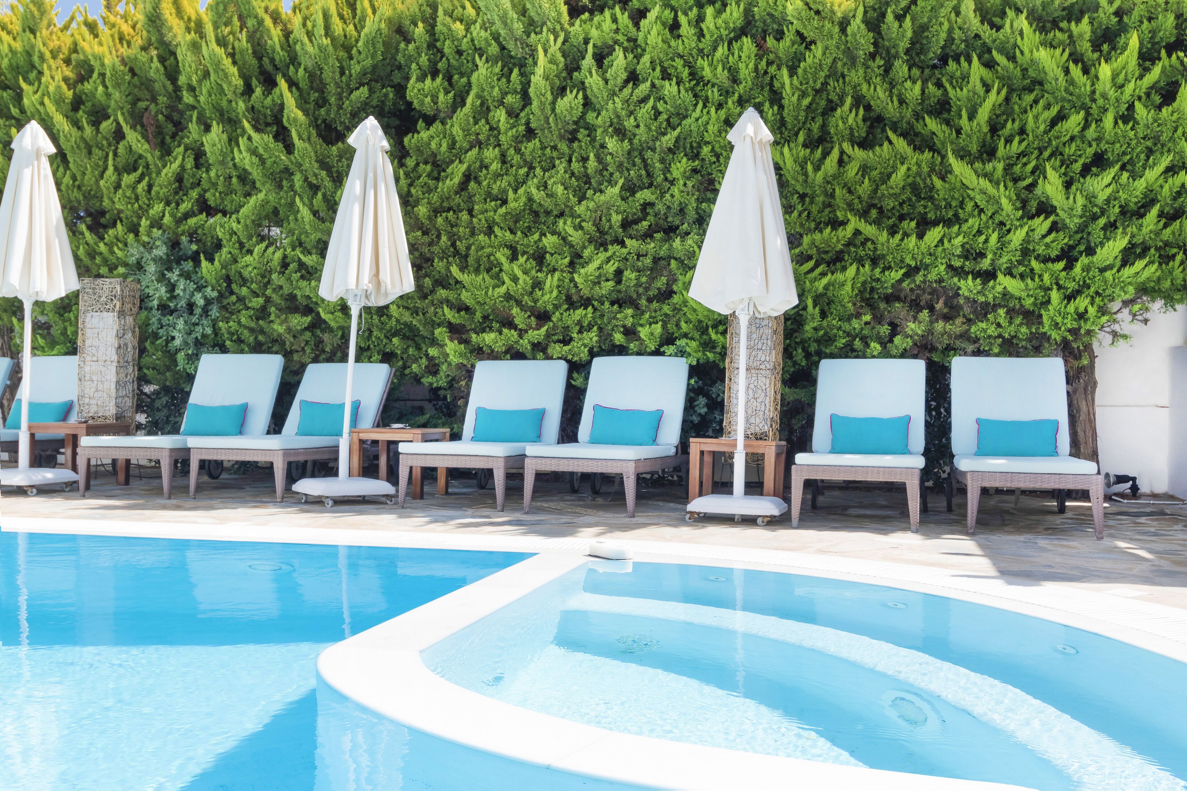 Un espace piscine agrémenté de chaises longues et de parasols, le tout entouré d’une haie.