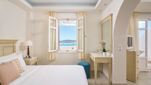 A hotel room with a bed, bedside table, lamp, and a view of the sea through an open window. - Stelia Mare Boutique Hotel (Paros)