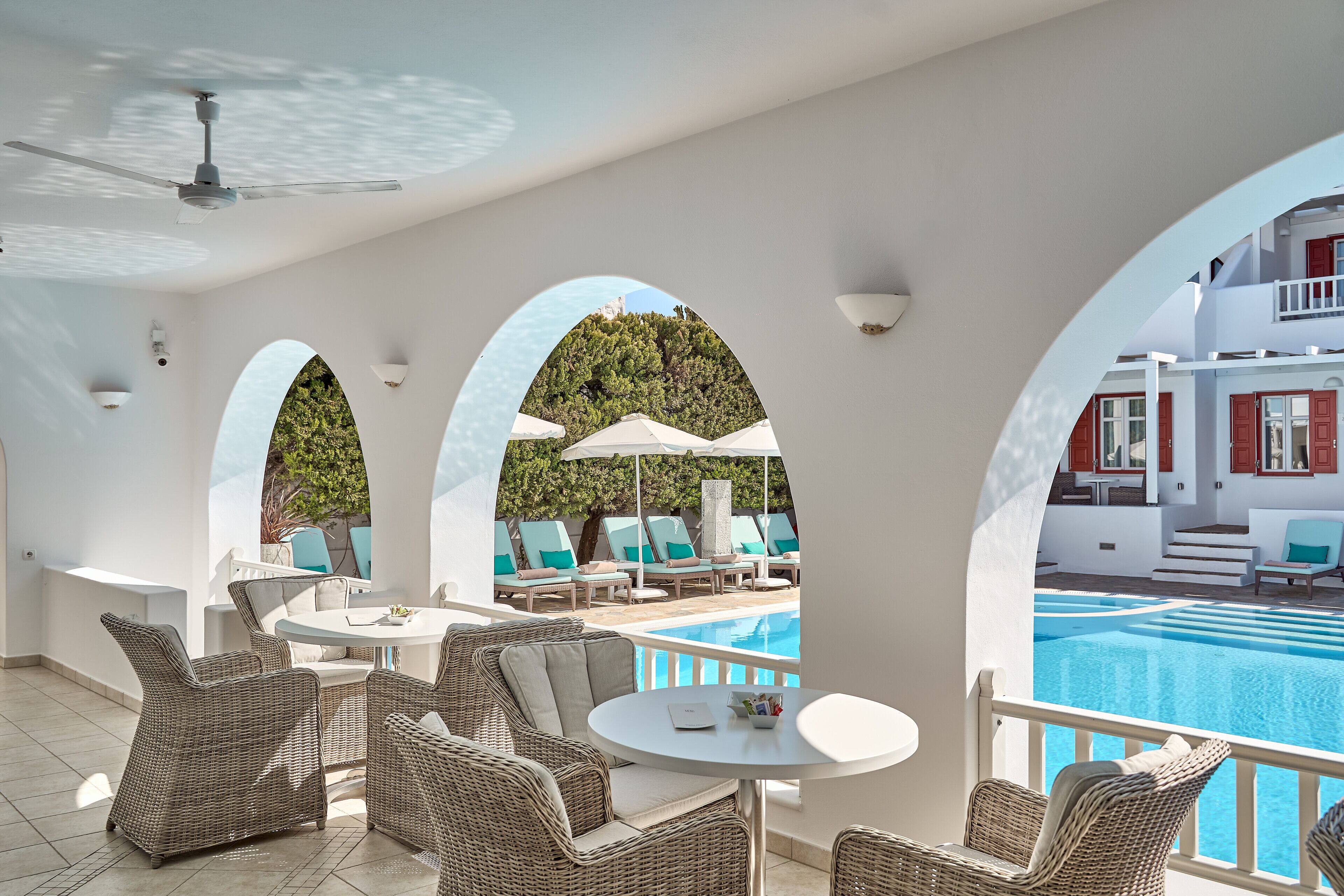 A poolside area with wicker furniture, a round table, and a view of a pool and outdoor seating.