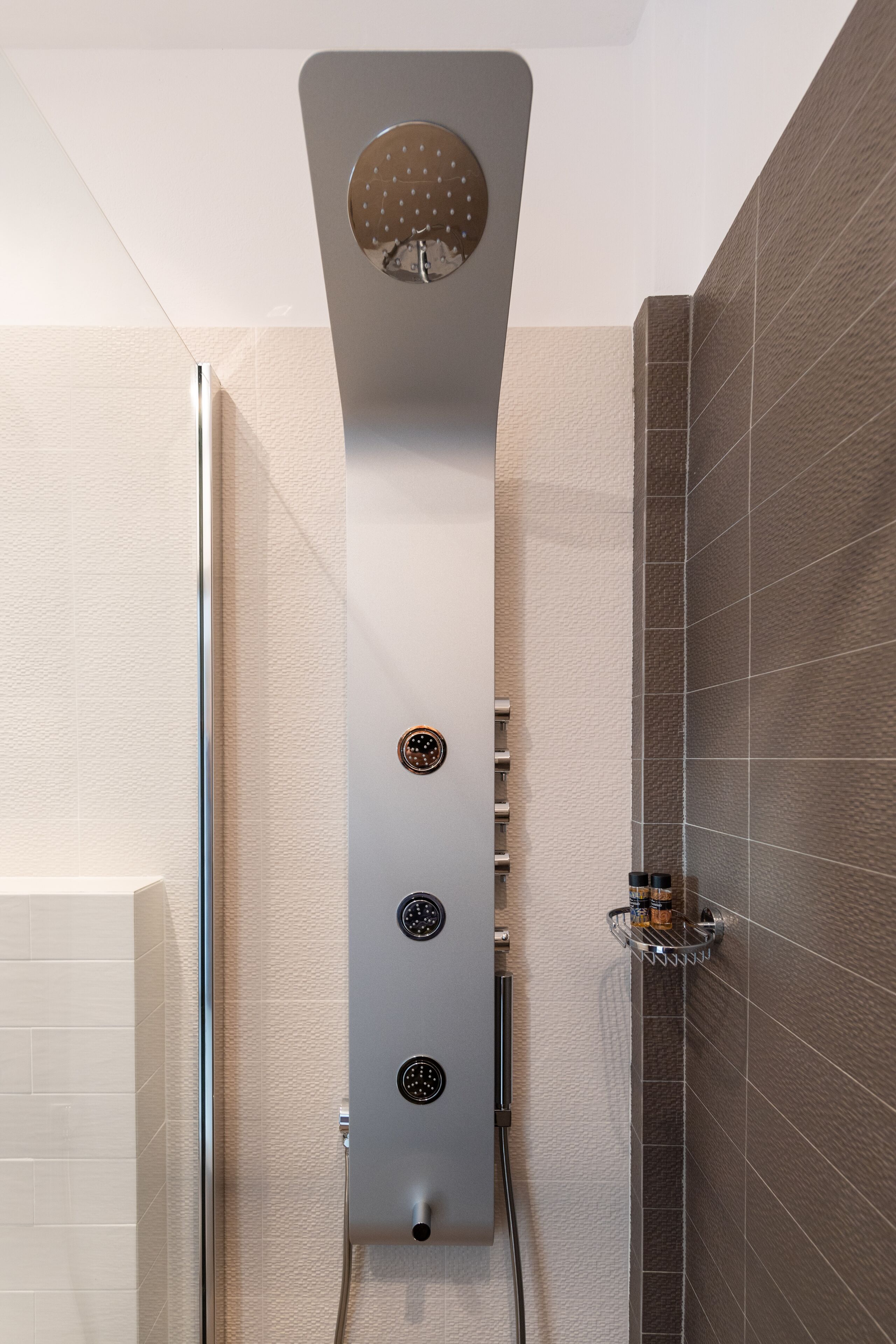 A modern shower with a rain showerhead, multiple control knobs, and a chrome shower tray.