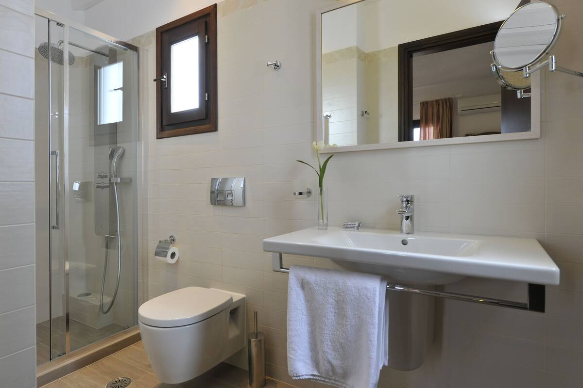 A modern bathroom with a glass-enclosed shower, a white toilet, a sink with a mirror, and a towel hanging on the wall.