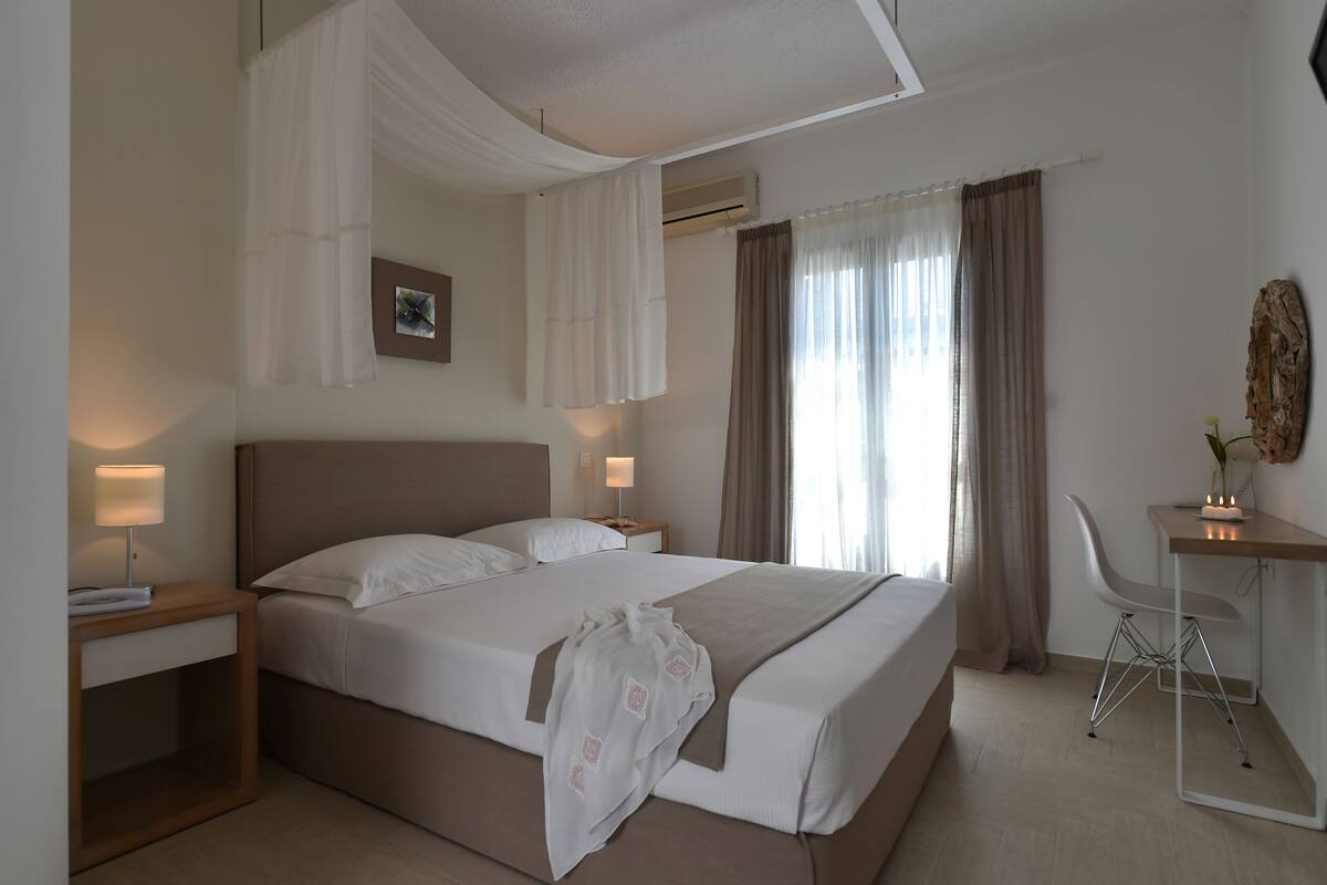 A hotel room with a large bed, bedside tables with lamps, a desk with a chair, and a window with curtains.