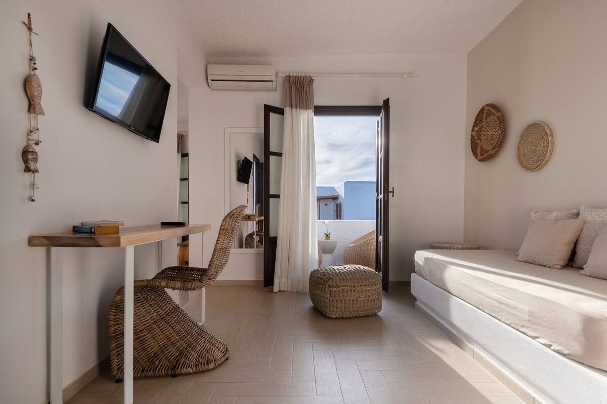A modern hotel room with a bed, a desk, a chair, and a TV.