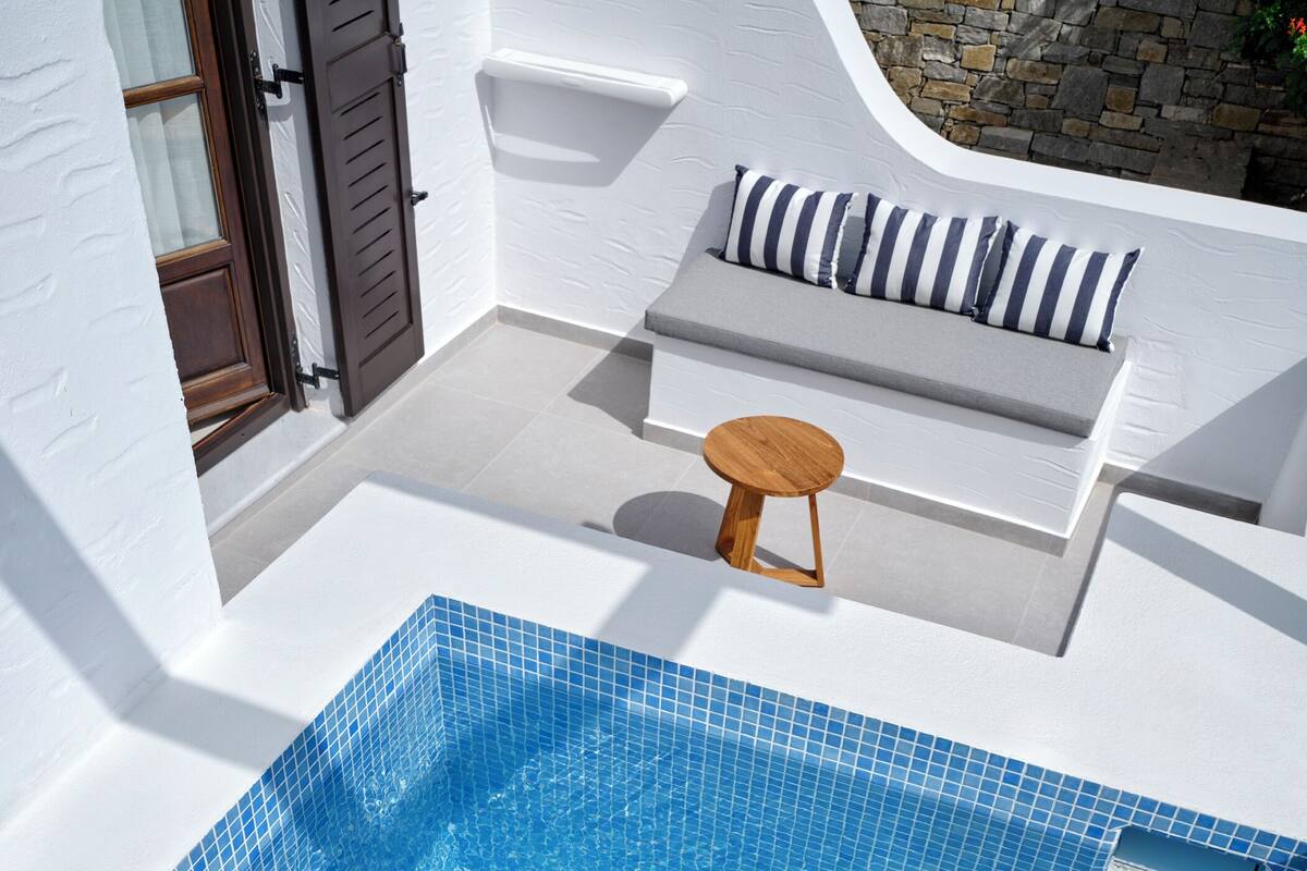 A modern outdoor pool area with a tiled blue pool, a wooden stool, and a seating area with cushions.