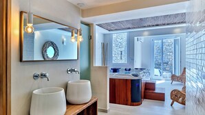 Un bagno moderno con due ampi lavabi, uno specchio e una panca in legno. Sullo sfondo, una vasca idromassaggio con vista sull'esterno.