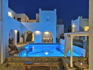 A pool area with a stone deck, lounge chairs, and a staircase leading to a rooftop terrace. - Aella Residence (Paros)