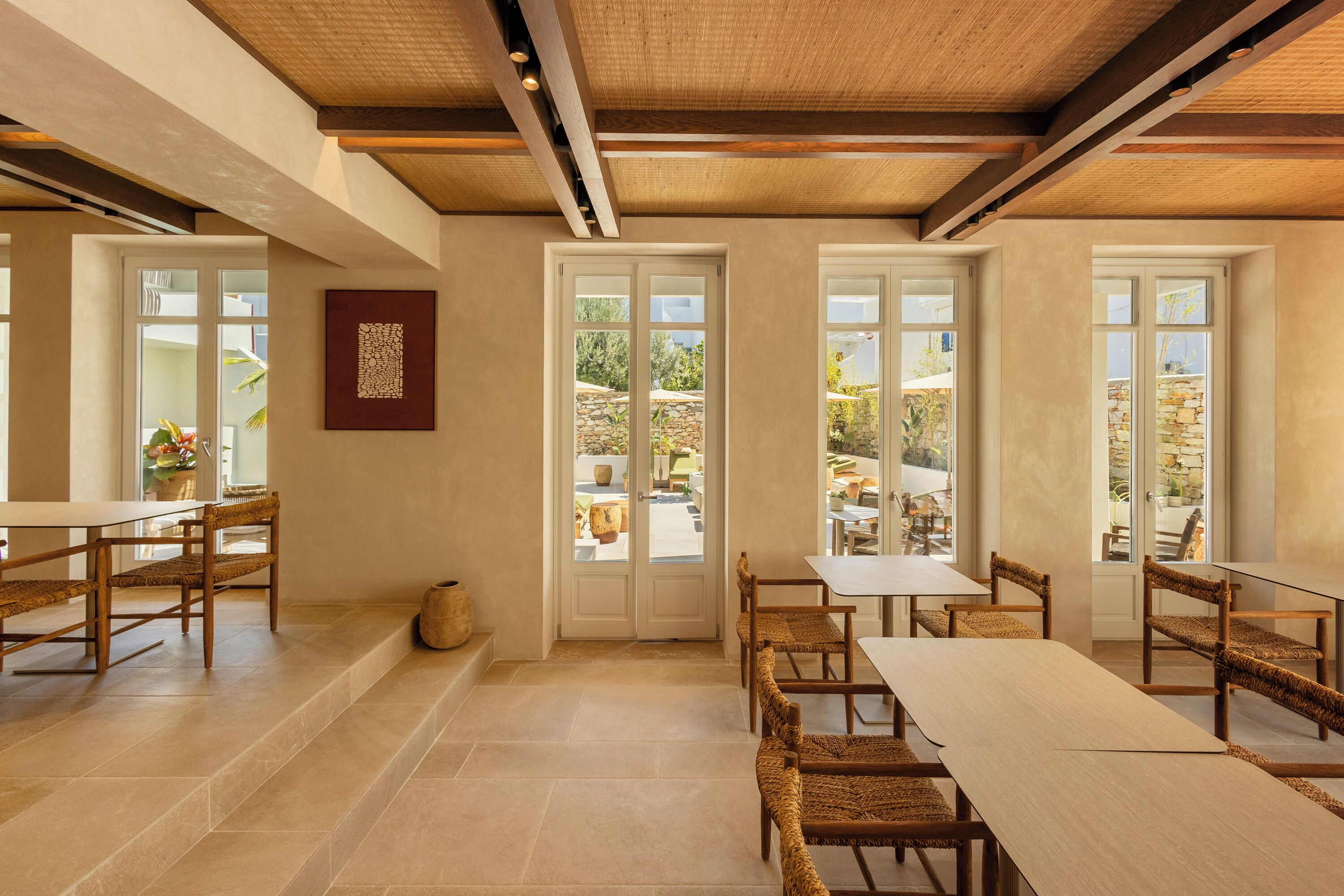 A dining area with a long table and chairs, large windows, and a view of the outdoors.