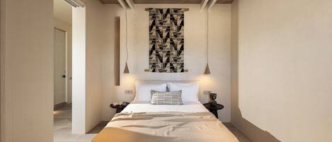 Une chambre à coucher avec un grand lit, une œuvre d’art abstraite suspendue au mur, deux tables de chevet et un tapis à motifs.