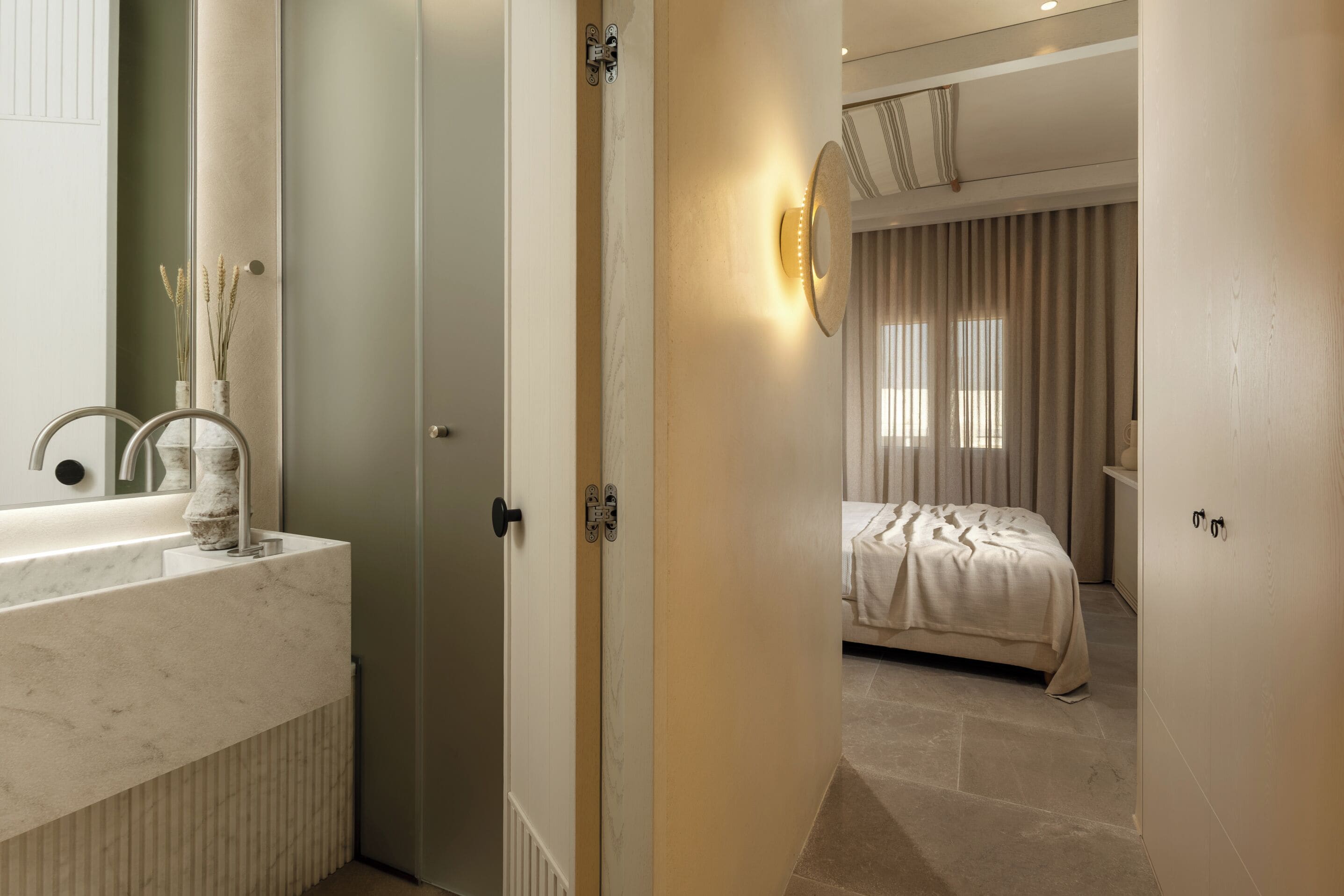 Een moderne badkamer met een marmeren wastafel, een spiegel en een vaas met gedroogde bloemen.