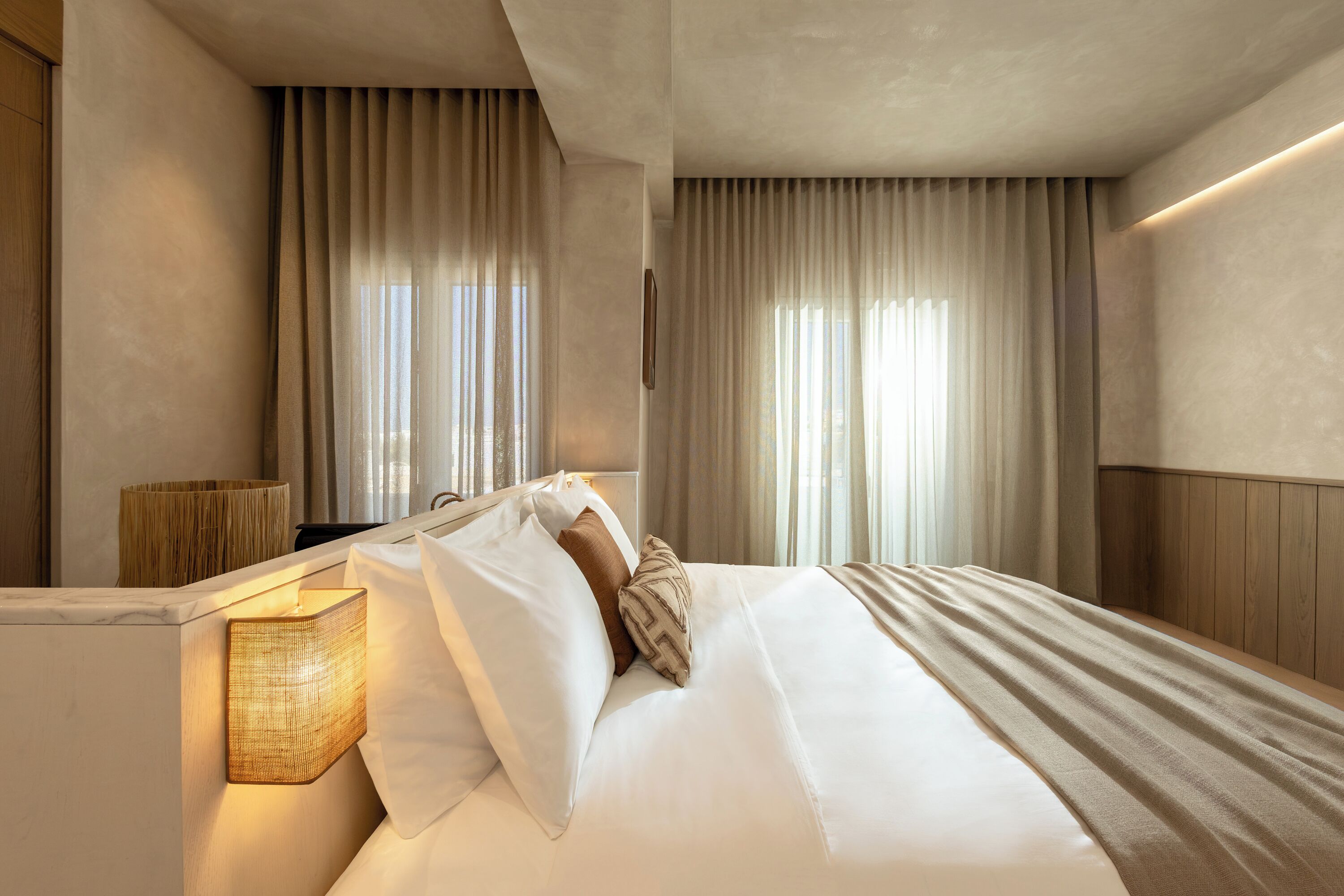 A hotel room with a bed, curtains, a lamp, and a wooden headboard.