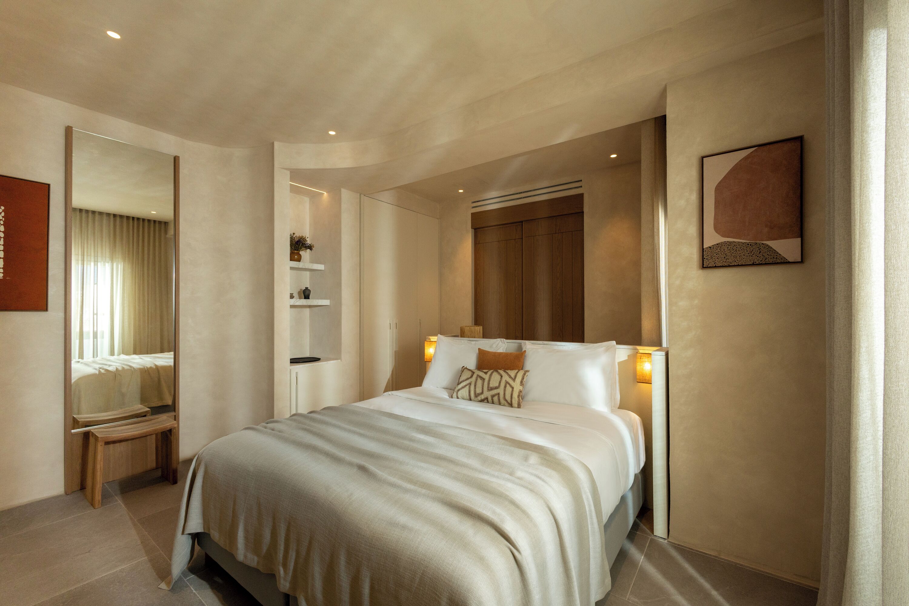 A modern hotel room with a large bed, bedside tables, a mirror, and a wall-mounted artwork.