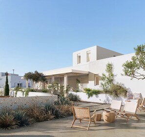 A modern outdoor seating area with chairs and a table, surrounded by plants and a white building.