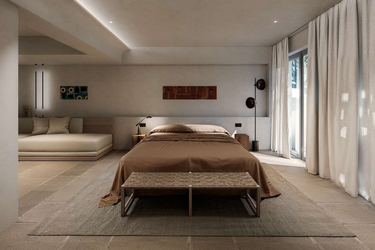 A modern bedroom with a large bed, a bench, a sofa, and a large window with curtains.