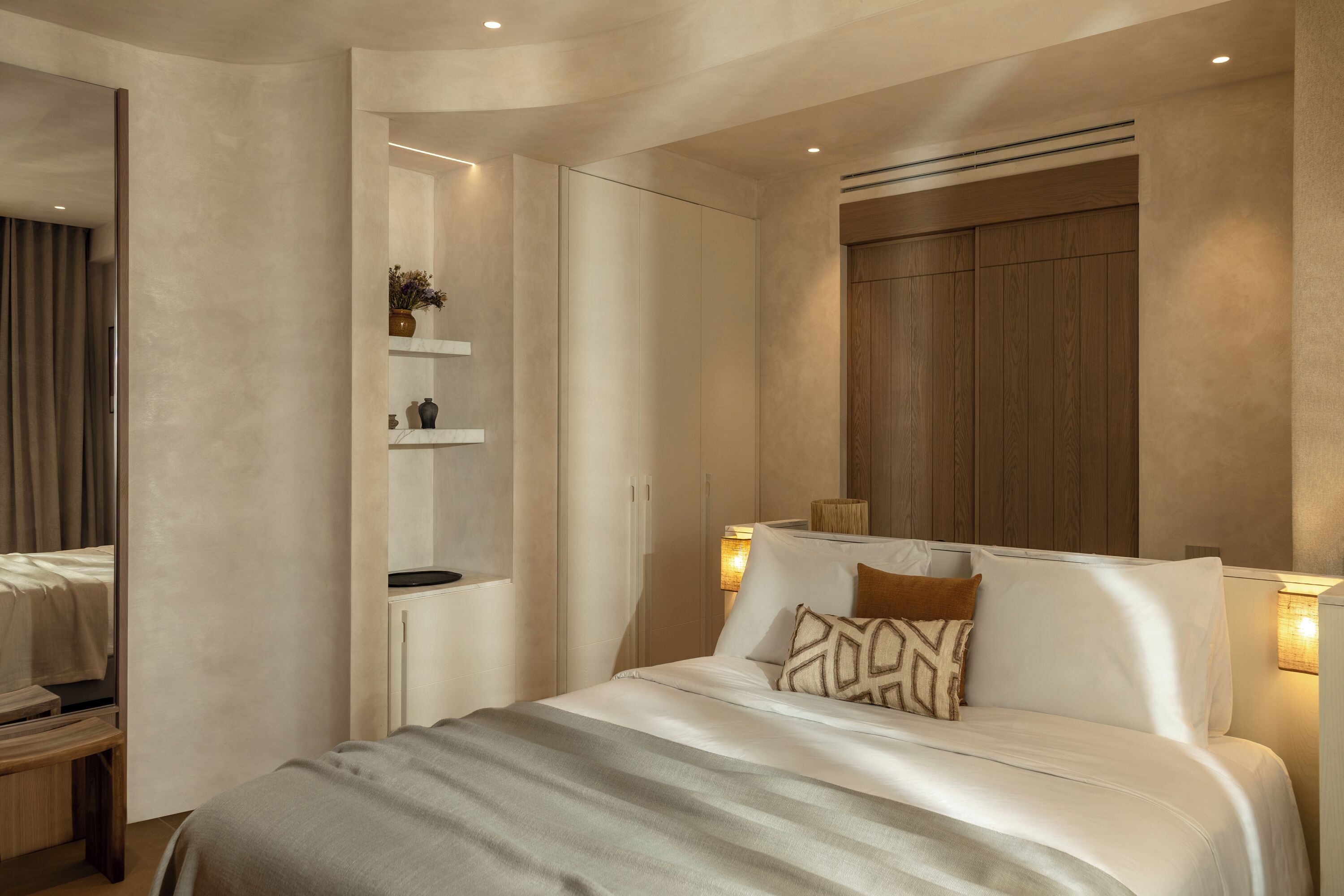A modern bedroom with a large bed, bedside lamps, a built-in shelf with decorative items, and a wooden headboard.