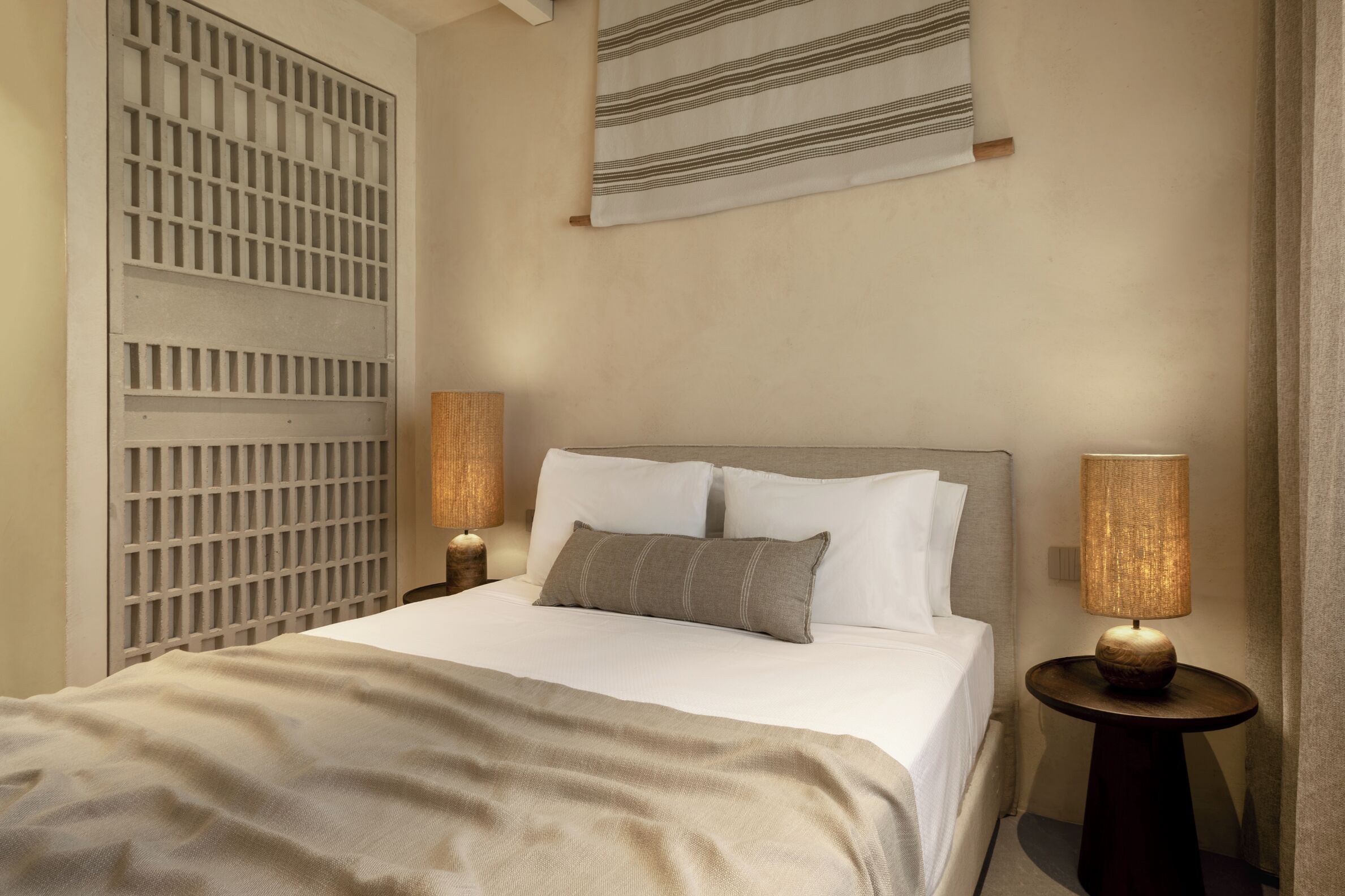 A bedroom with a bed, two bedside lamps, a wall-mounted lamp, and a window with a white blind.