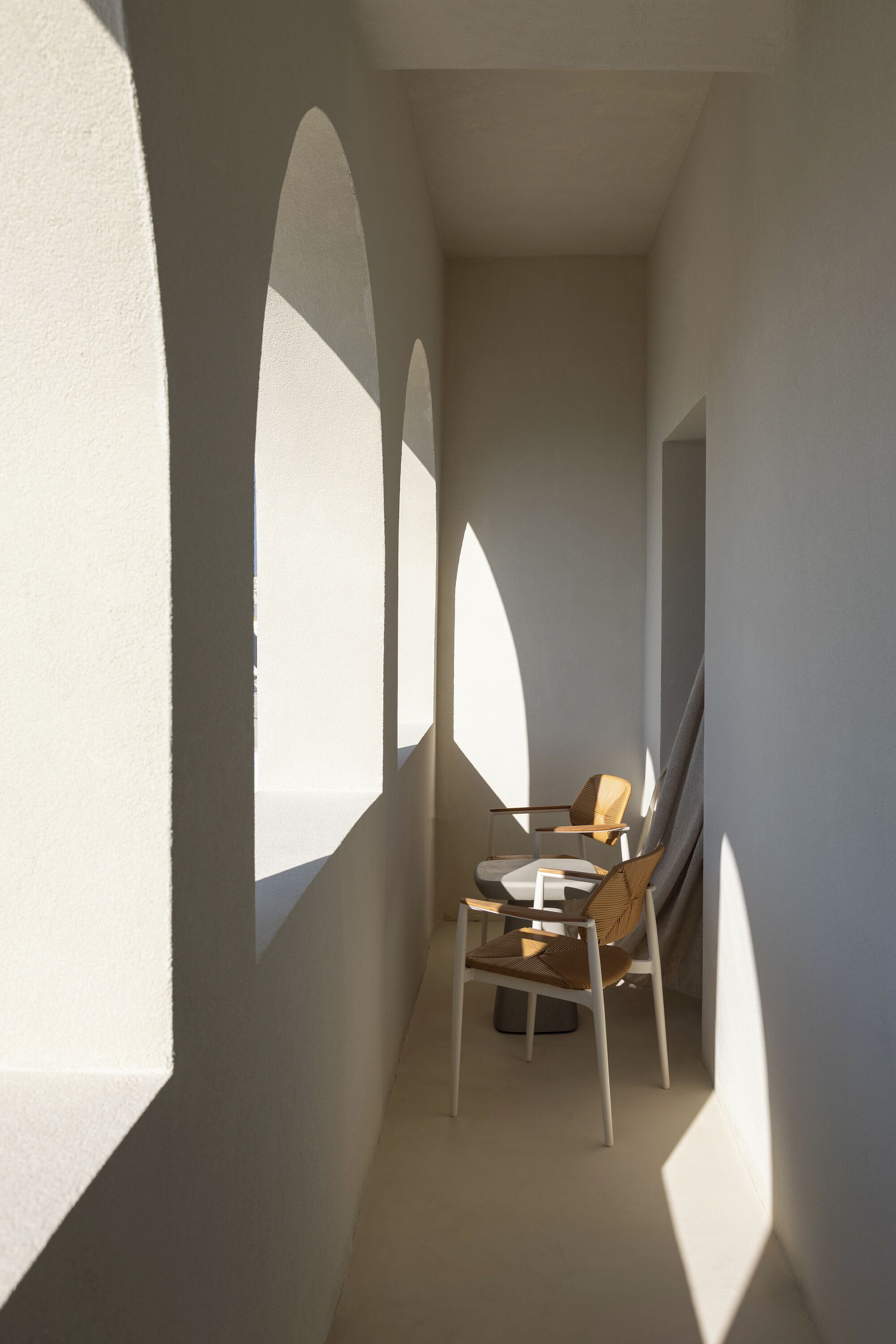 A narrow hallway with arched windows and a chair.