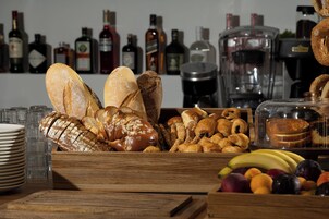 Diversa variedad de panes y pasteles sobre una mesa de madera, con botellas y una máquina de café al fondo.