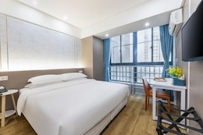 A hotel room with a large bed, a desk, a chair, and a window with curtains.
