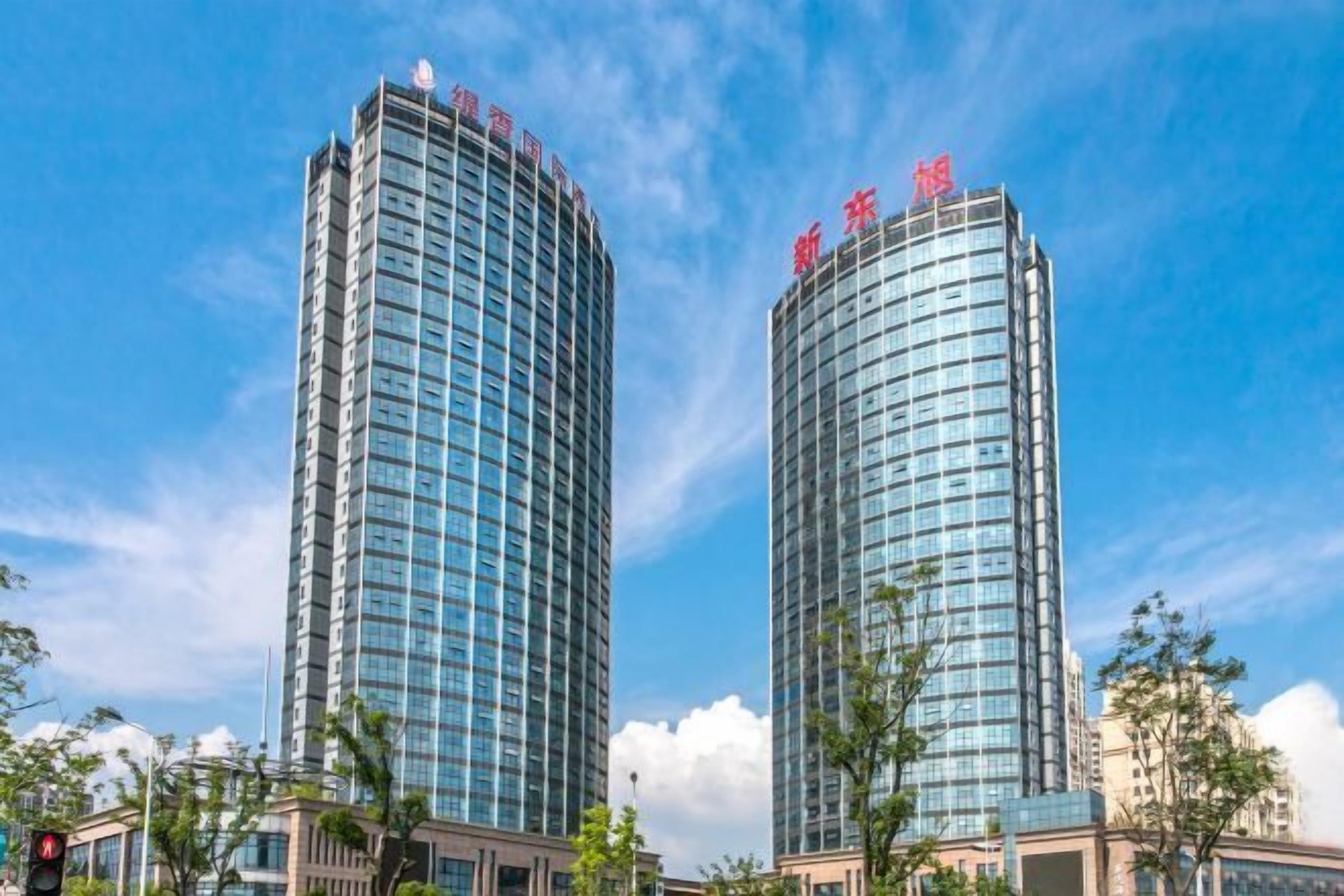 Two high-rise buildings with reflective glass facades and red signage at the top.
