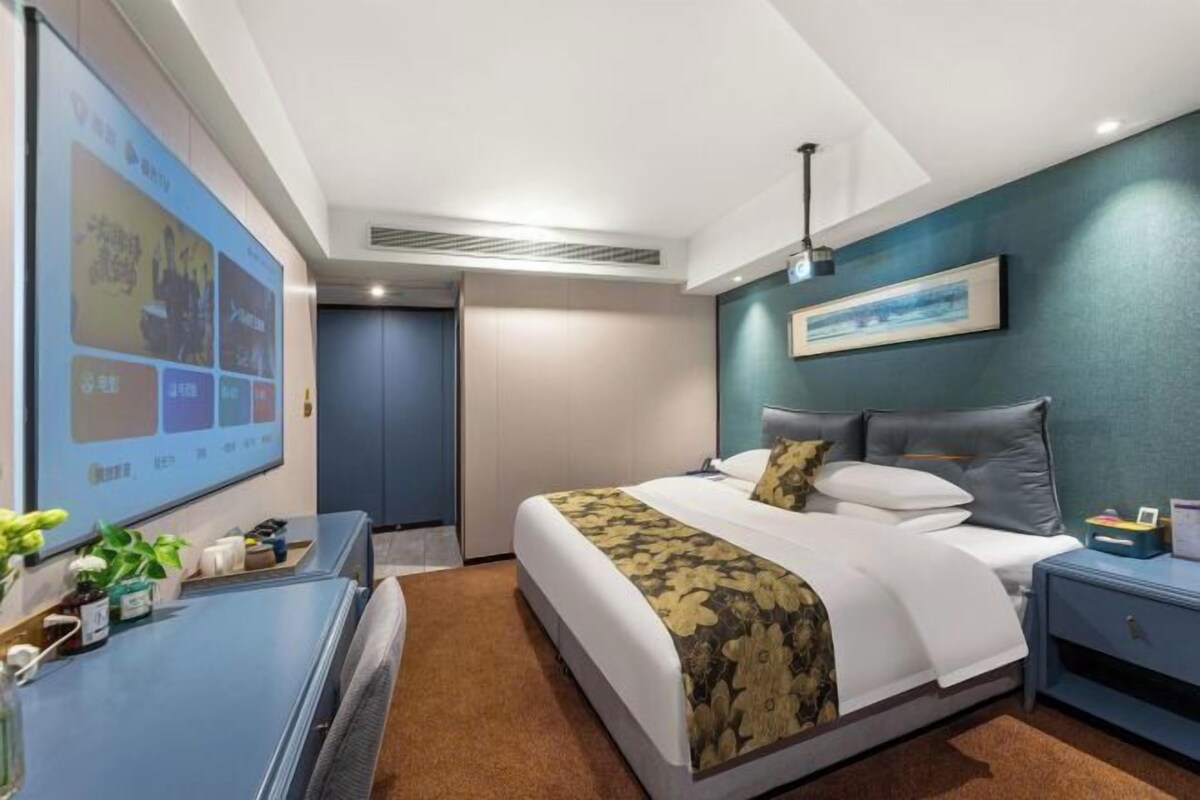 A hotel room with a bed, bedside table, and a large screen displaying content.