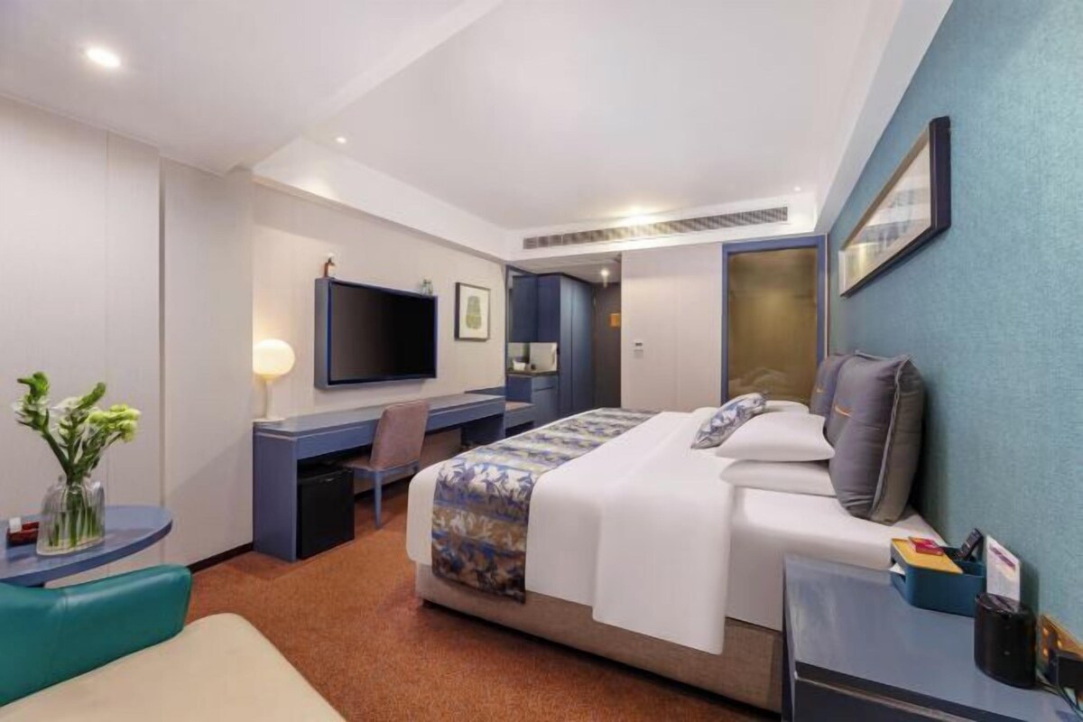 A hotel room with a bed, desk, chair, TV, and a small table with a vase of flowers.
